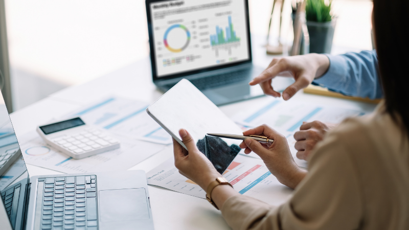Two people reviewing reports on cash vs. accrual accounting while using a tablet, laptop, calculator, and graphs on a table.