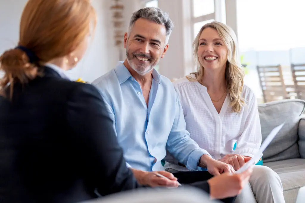 Happy mature couple meeting investments and financial advisor at home. They are happy and smiling sitting in the living room discussing estate, trust, and gift planning.